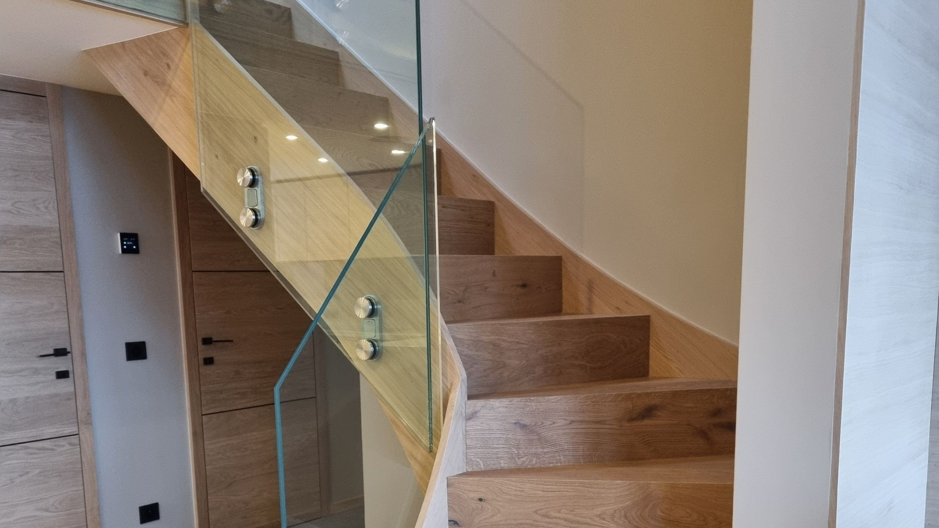 Escalier en bois avec rampe en verre. Des appliques murales éclairent les marches.