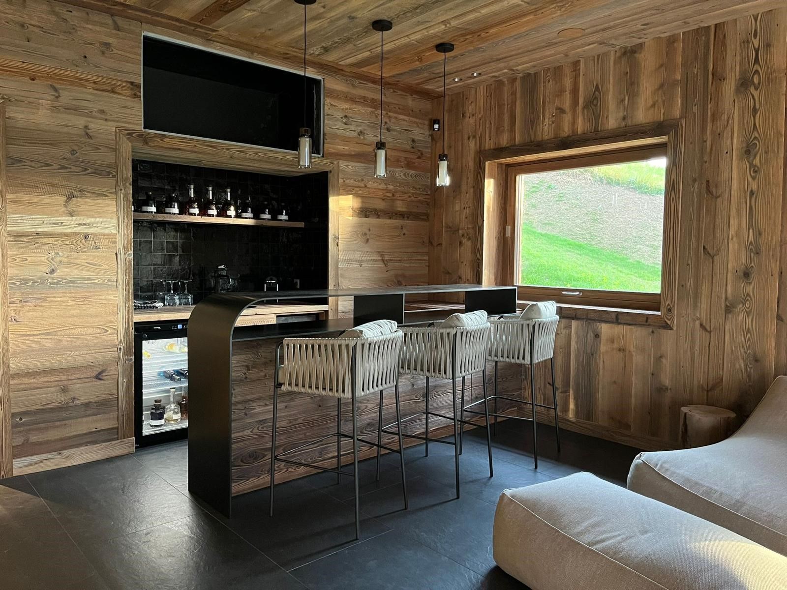 Coin bar avec murs en bois, tabourets de bar, fenêtre et fauteuils.