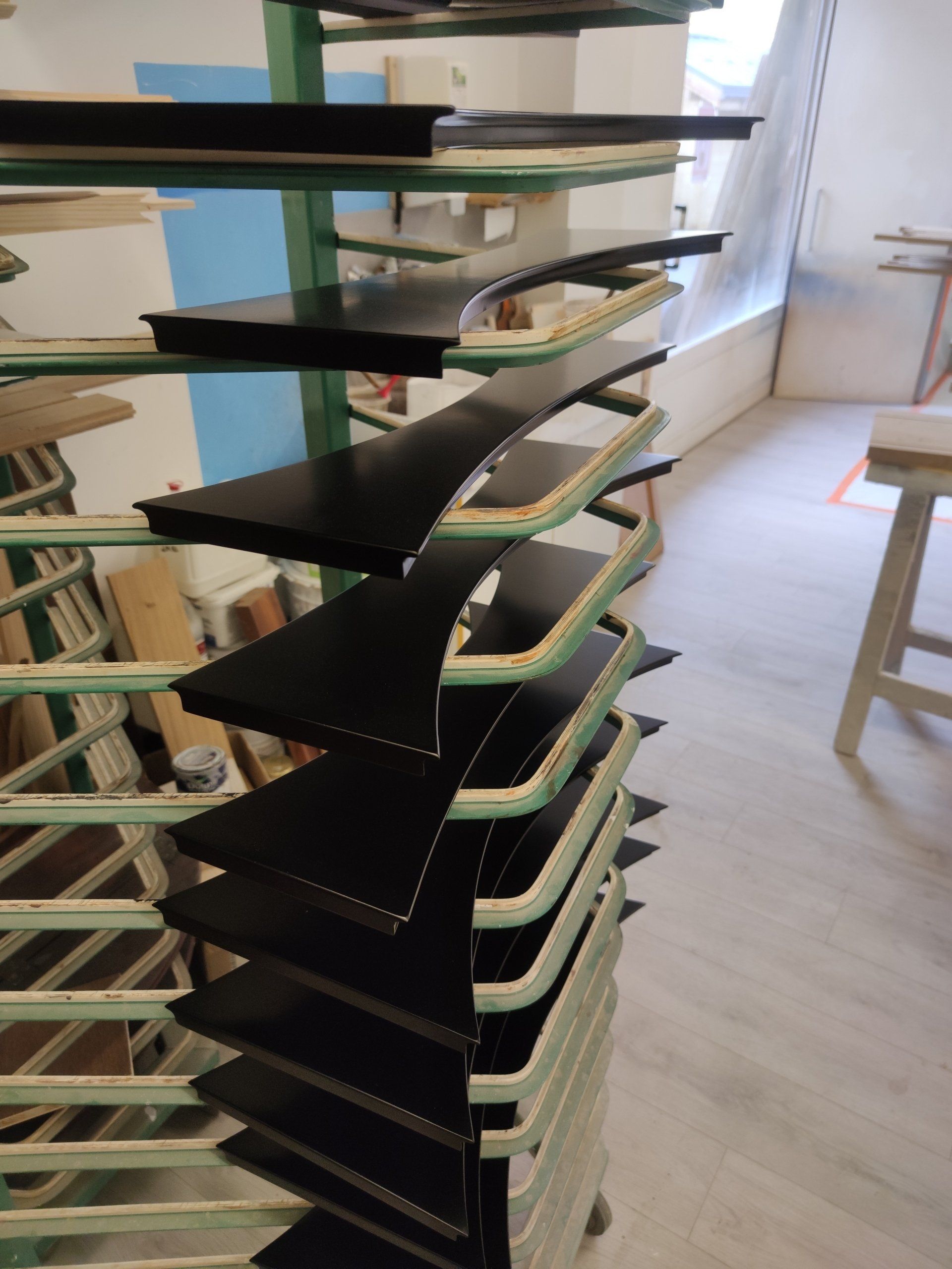 Des étagères noires et vert clair supportent des objets noirs et vert clair disposés en couches successives, à l'intérieur d'un atelier.