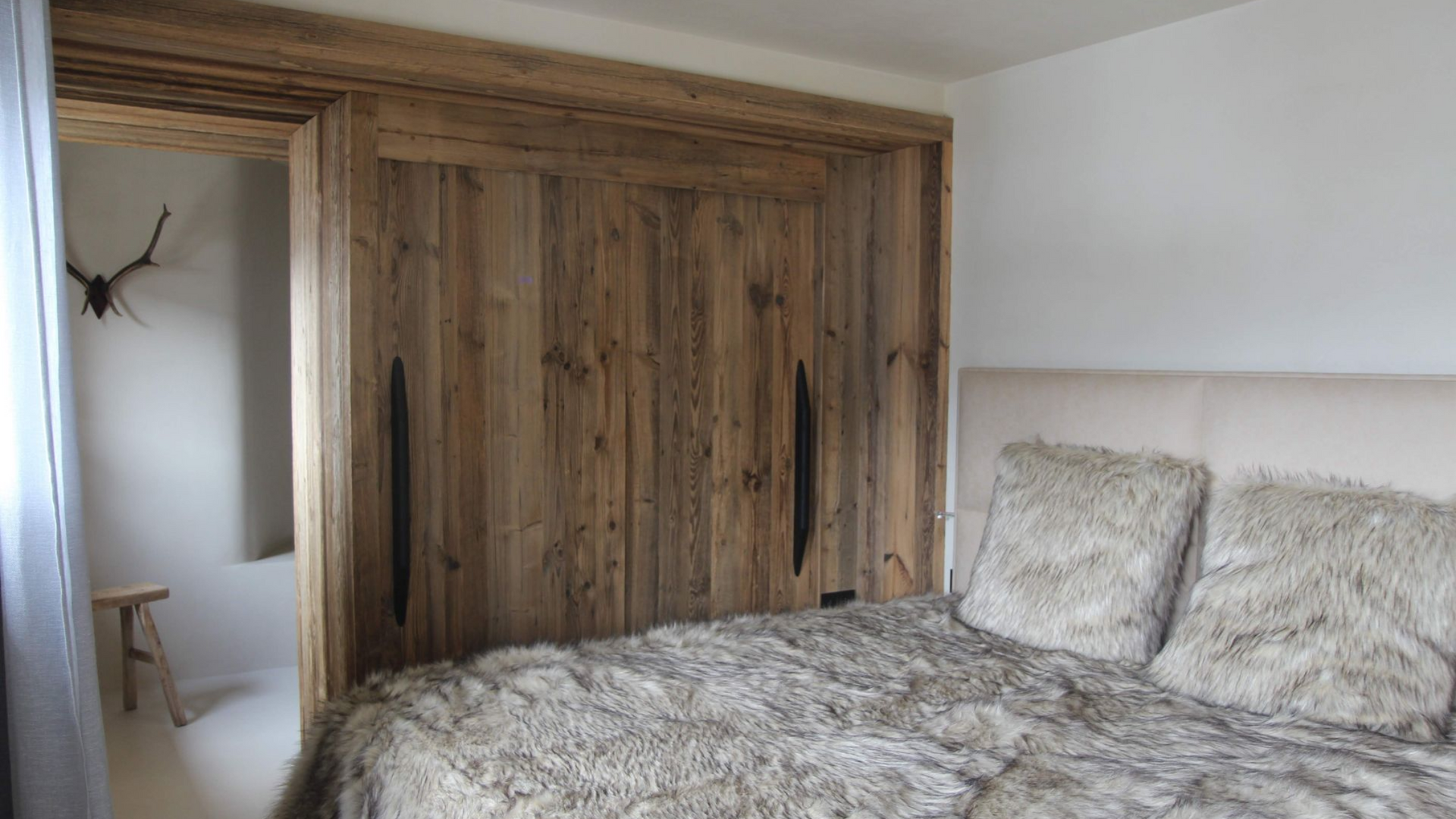Armoire en bois encastrée dans le mur d'une chambre, partiellement ouverte, avec un lit au premier plan.;