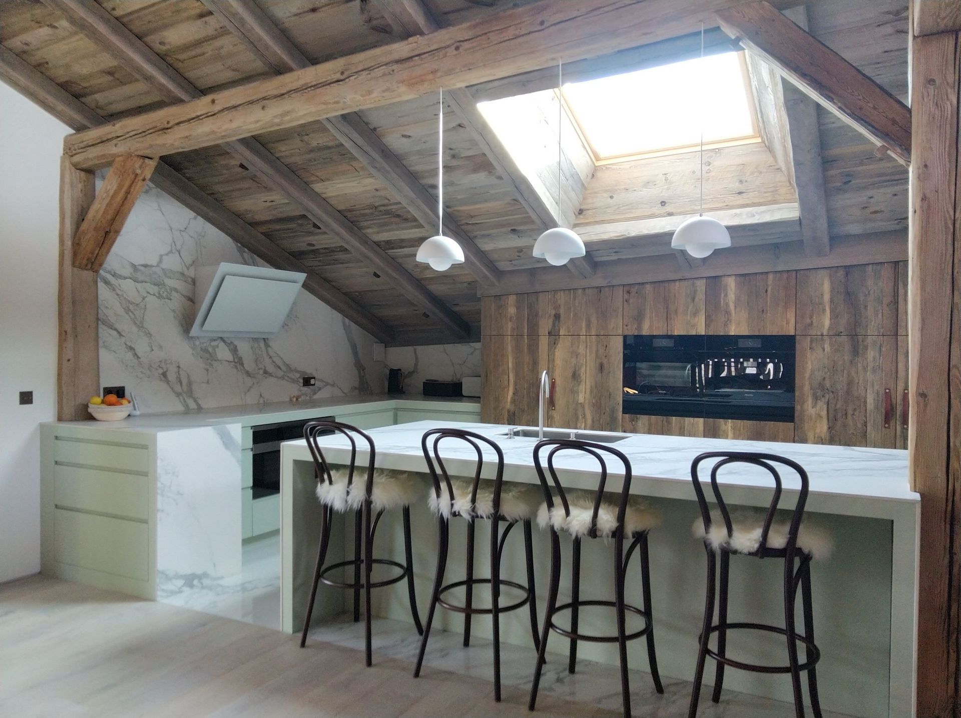 Cuisine moderne avec comptoirs vert clair, poutres en bois au plafond et tabourets de bar.