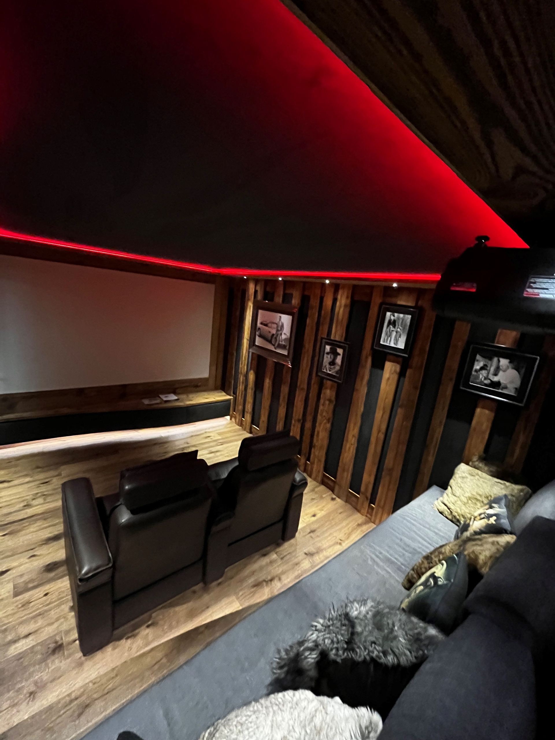 Salle de cinéma maison confortable avec éclairage rouge, boiseries, sièges en cuir noir et écran blanc.