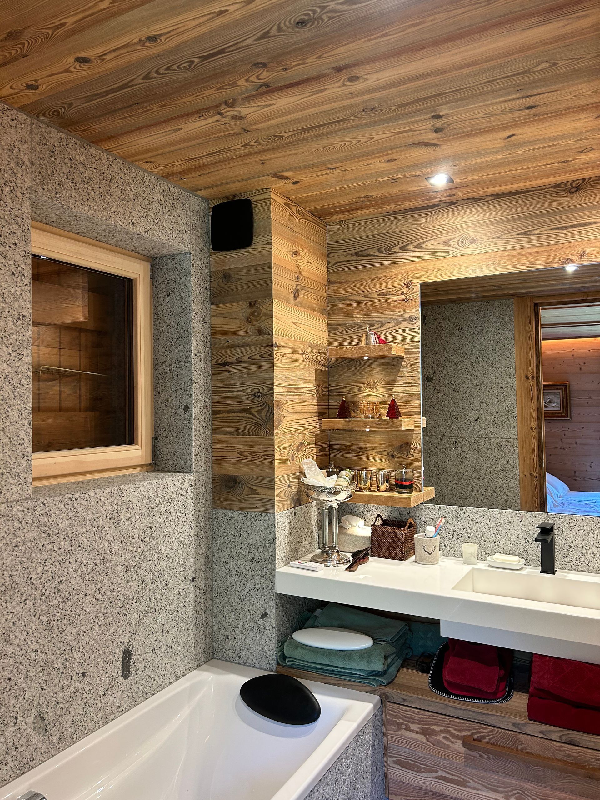 Salle de bains avec plafond lambrissé, murs texturés, fenêtre, lavabo blanc et baignoire.