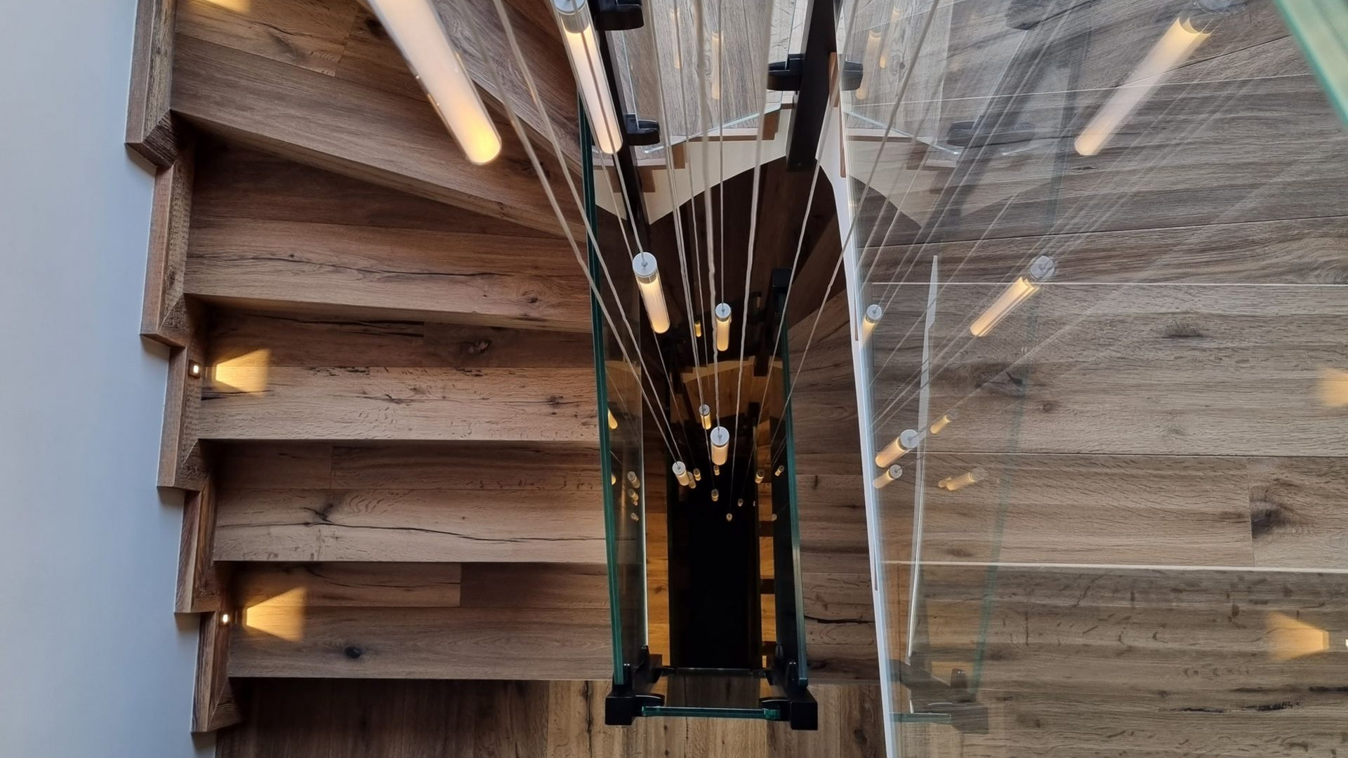 Escalier en colimaçon en bois avec rambarde en verre et éclairage intégré. Vue de dessus.