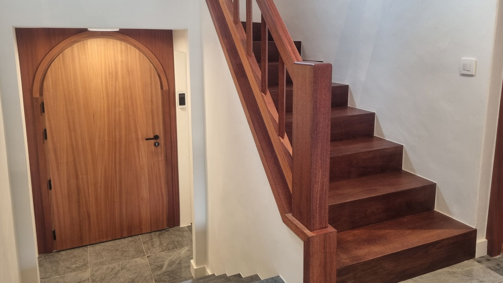 Porte et escalier en bois avec marches et rampe marron foncé. Murs blancs.