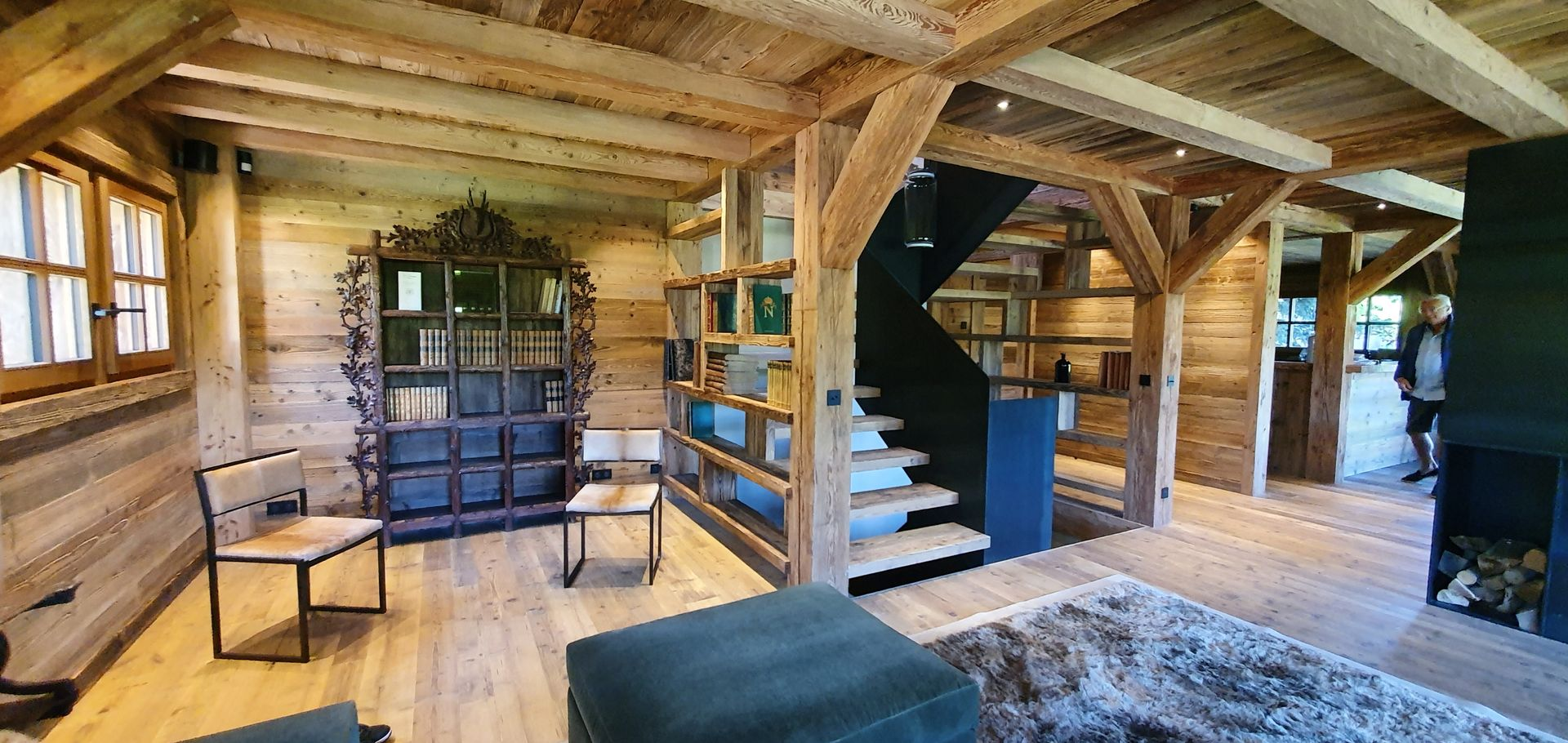 Intérieur en bois avec bibliothèque intégrée, un escalier et un coin salon avec tapis et chaises.