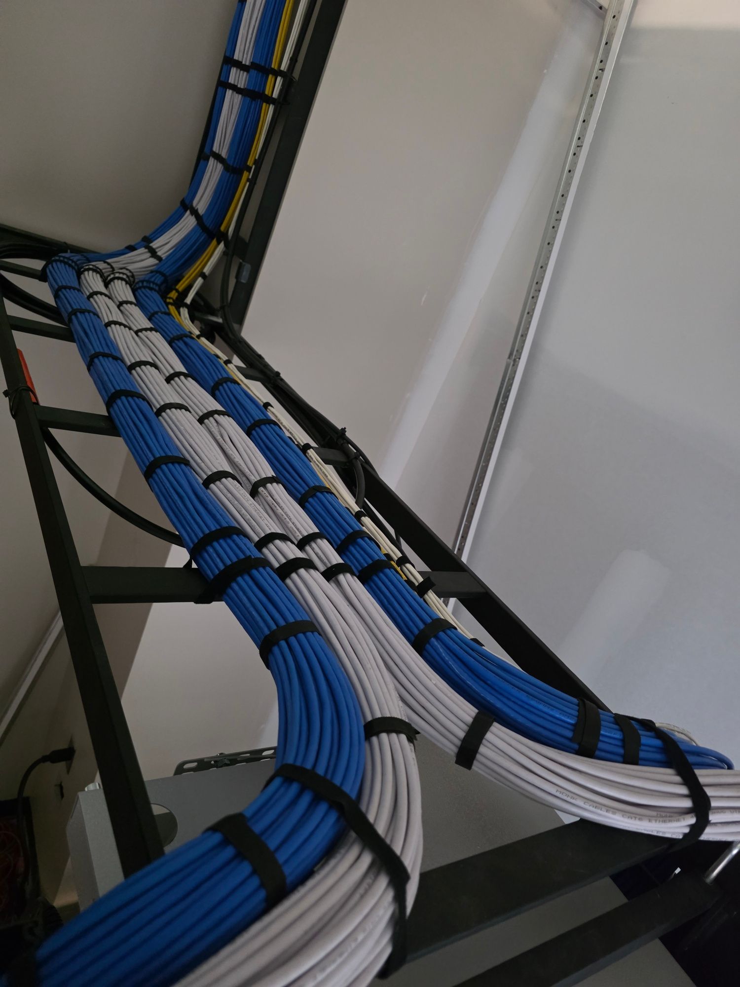 Neatly bundled multicolored cables routed around a white wall corner with cable clips.
