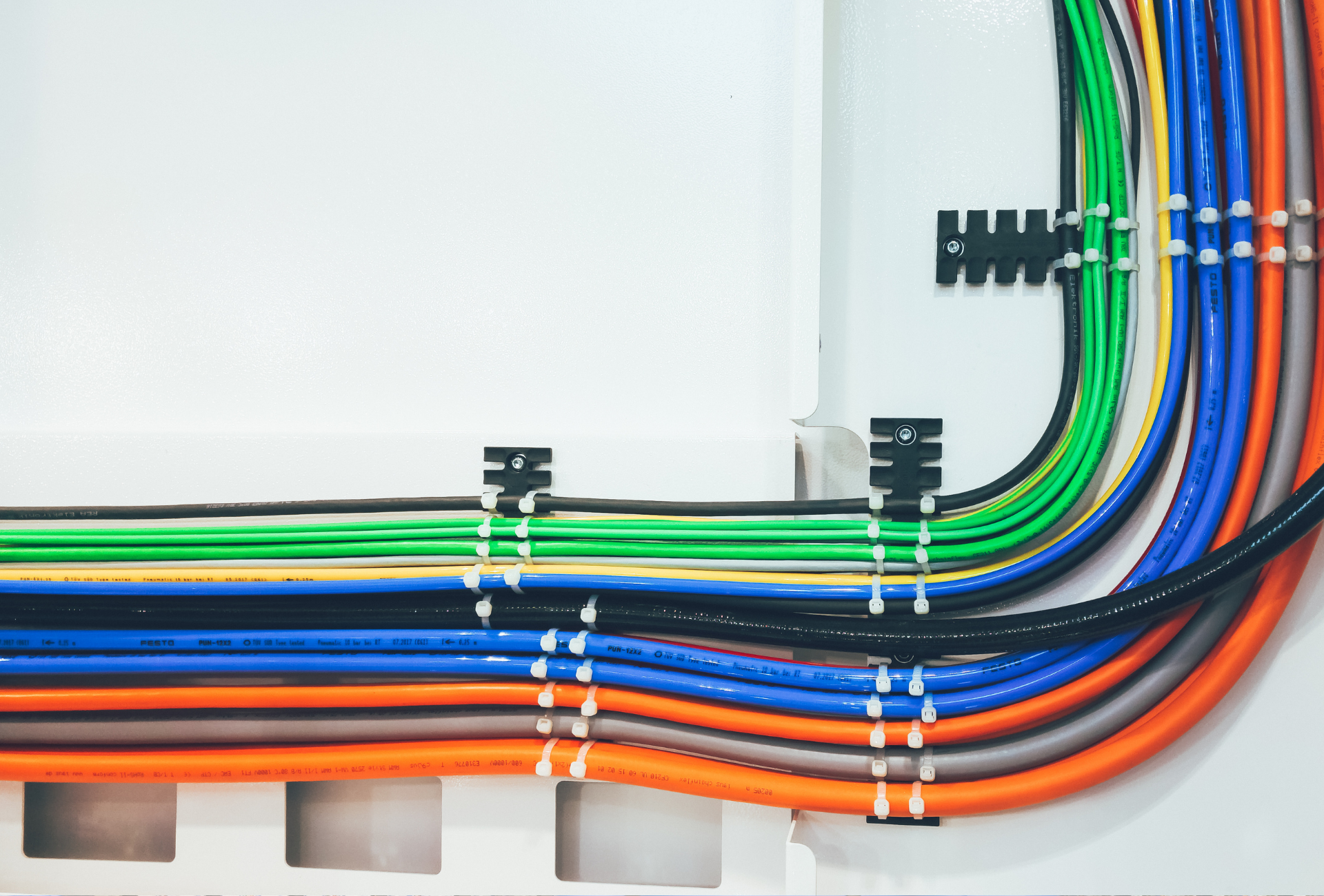 Neatly bundled multicolored cables routed around a white wall corner with cable clips.