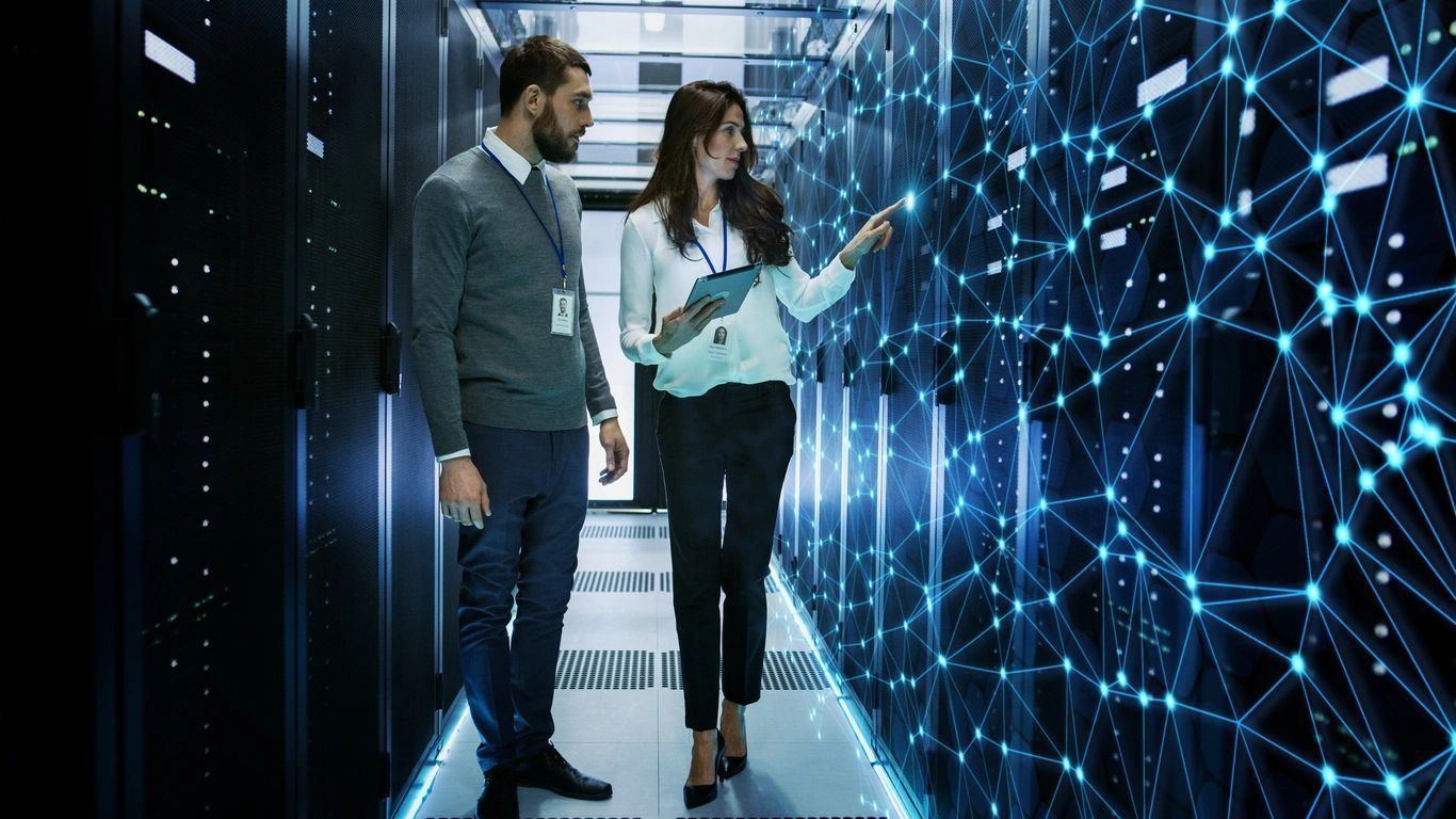 Two people in a server room reviewing digital network visuals on glowing screens
