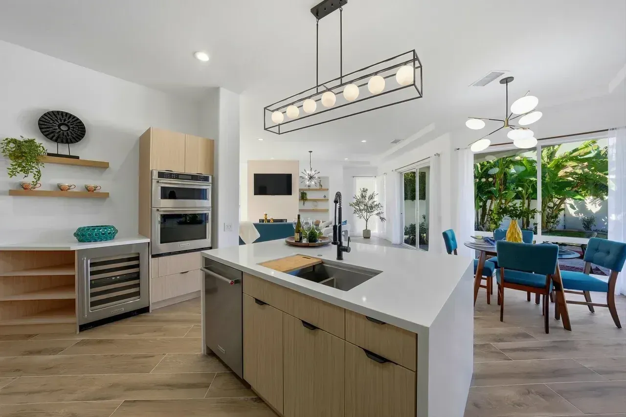 Modern kitchen with island, light wood cabinets, stainless steel appliances, and a dining area.