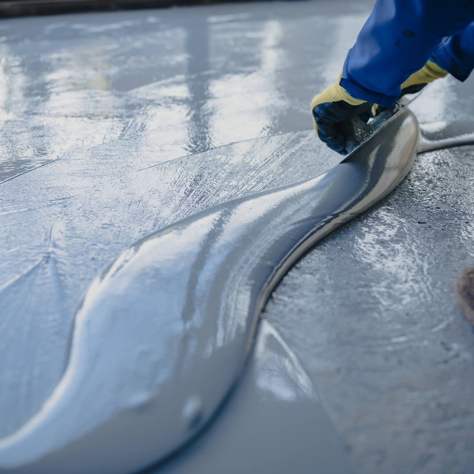 Person in blue gloves smoothing gray sealant on a floor.