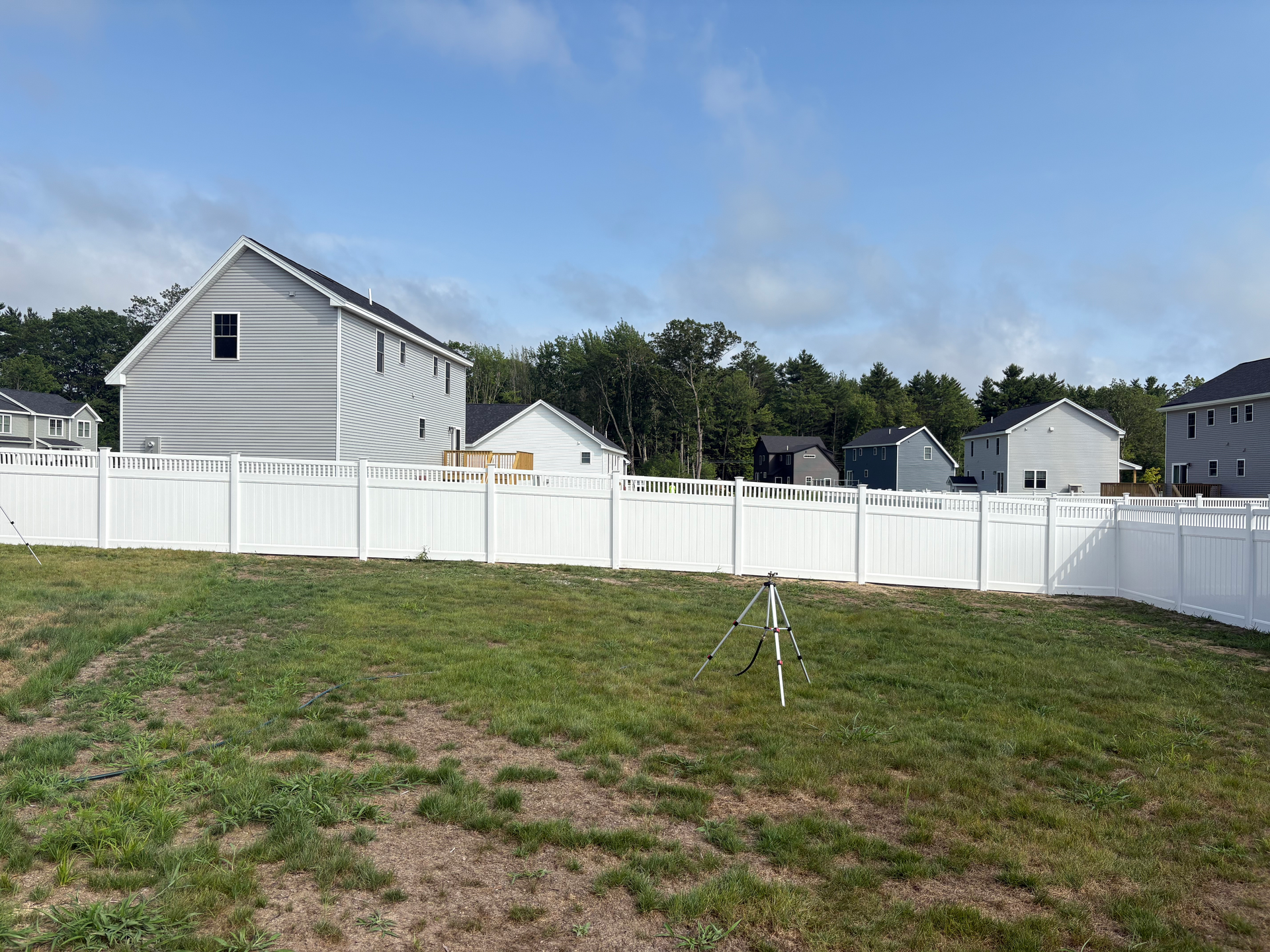 A white fence surrounds a lush green field with a house in the background.