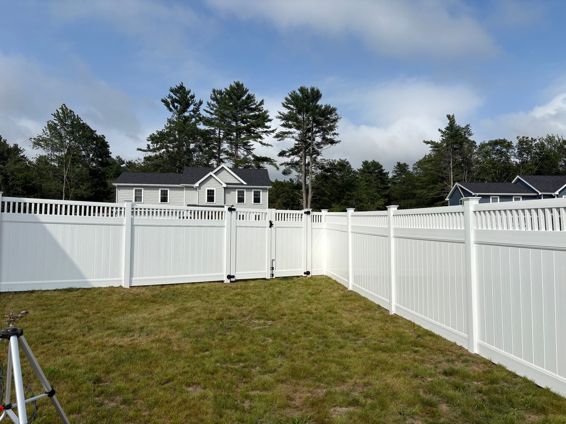 A white fence surrounds a grassy yard in front of a house.