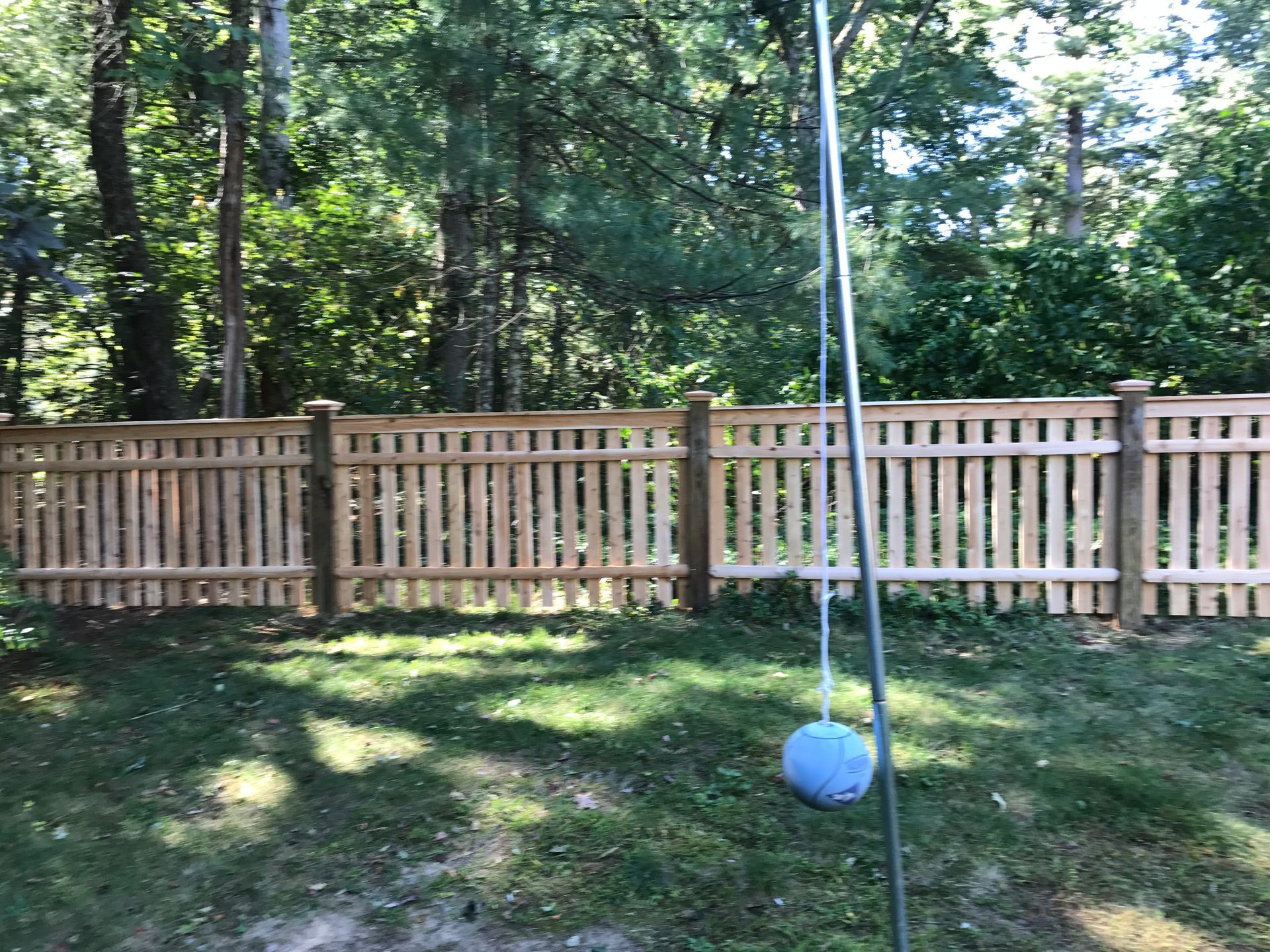 A wooden fence surrounds a backyard with trees in the background.
