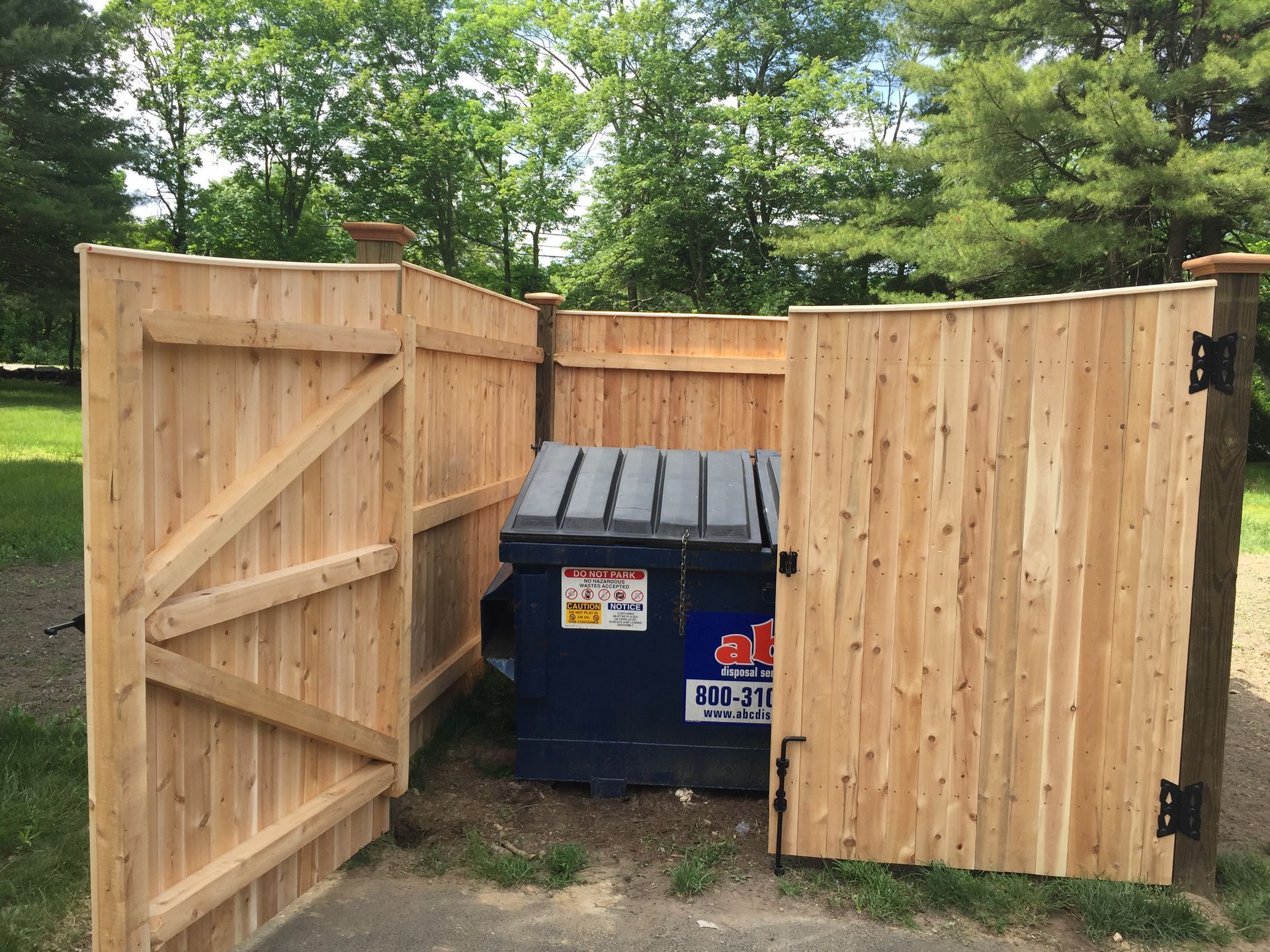 A dumpster is behind a wooden fence with the doors open
