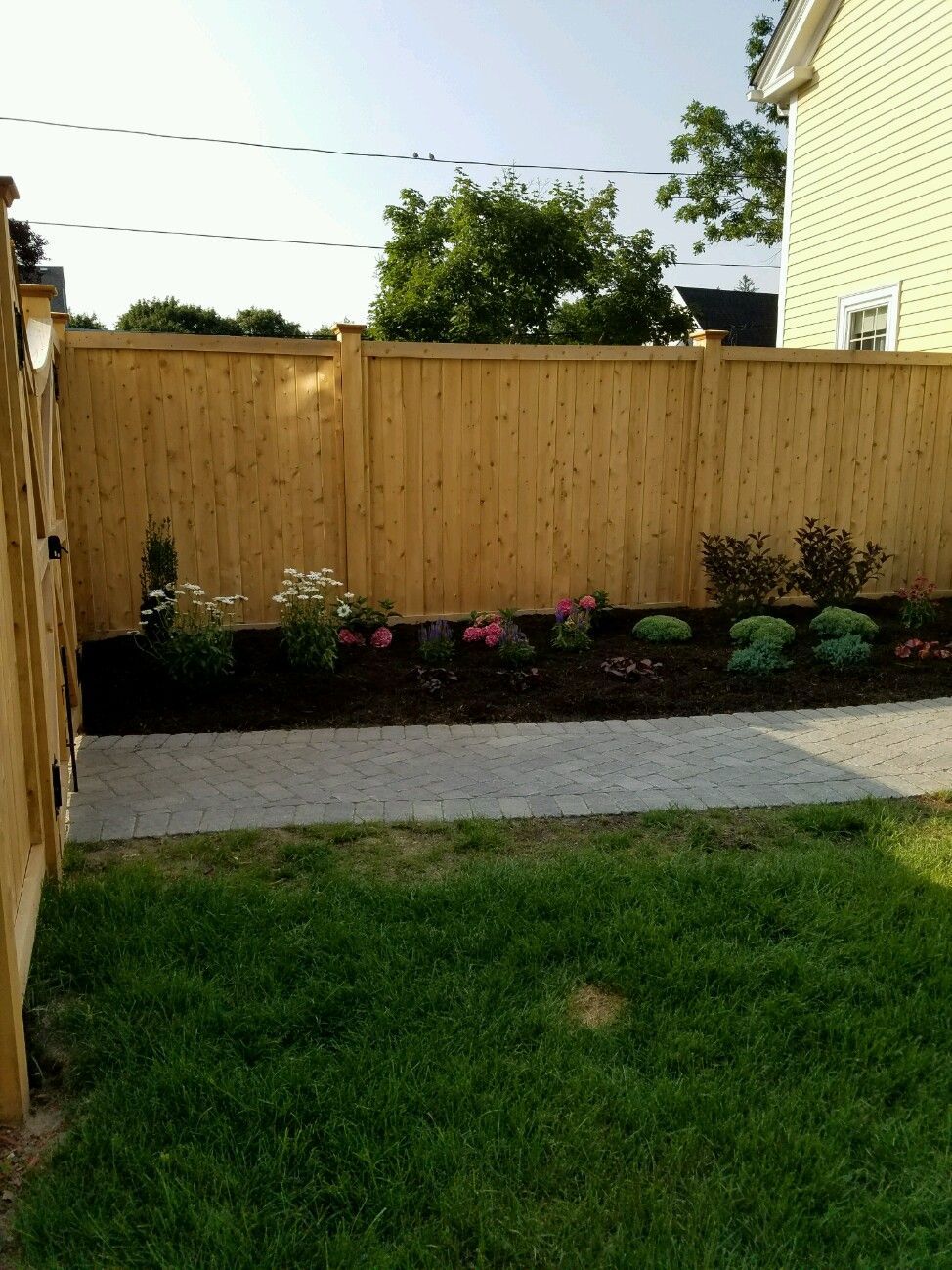 A wooden fence surrounds a lush green yard with flowers.