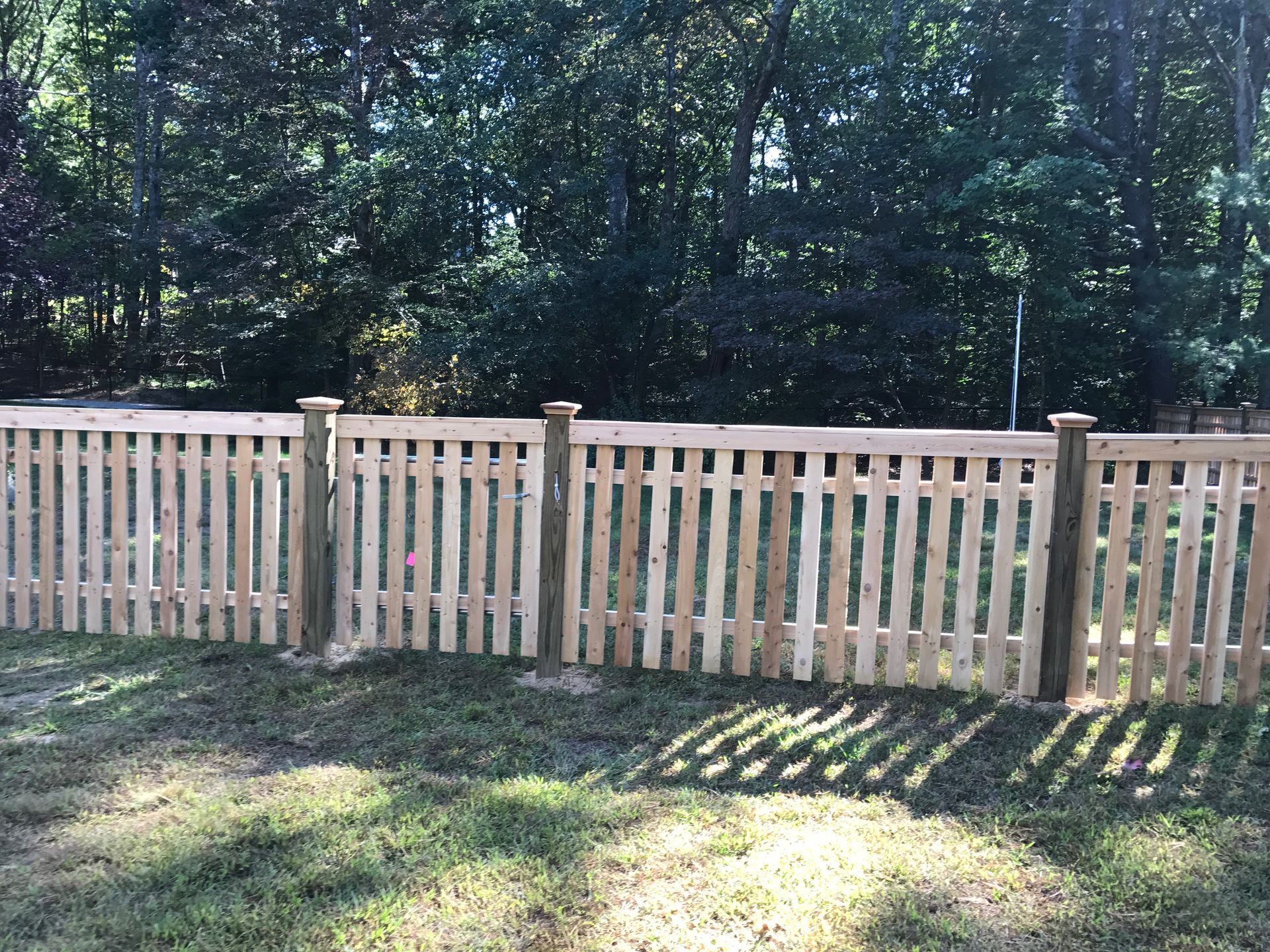 A wooden picket fence is in the middle of a lush green field.