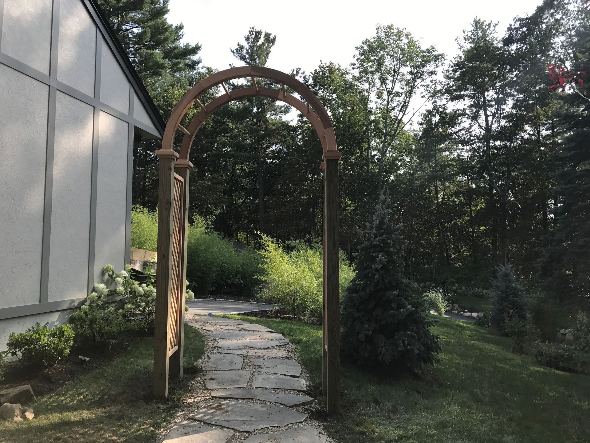 A wooden archway with a stone walkway leading to a house