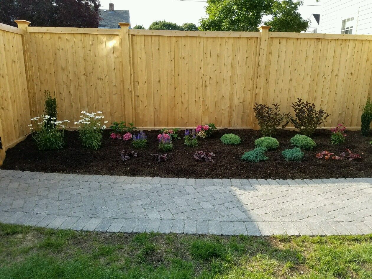 A wooden fence surrounds a garden with flowers and plants