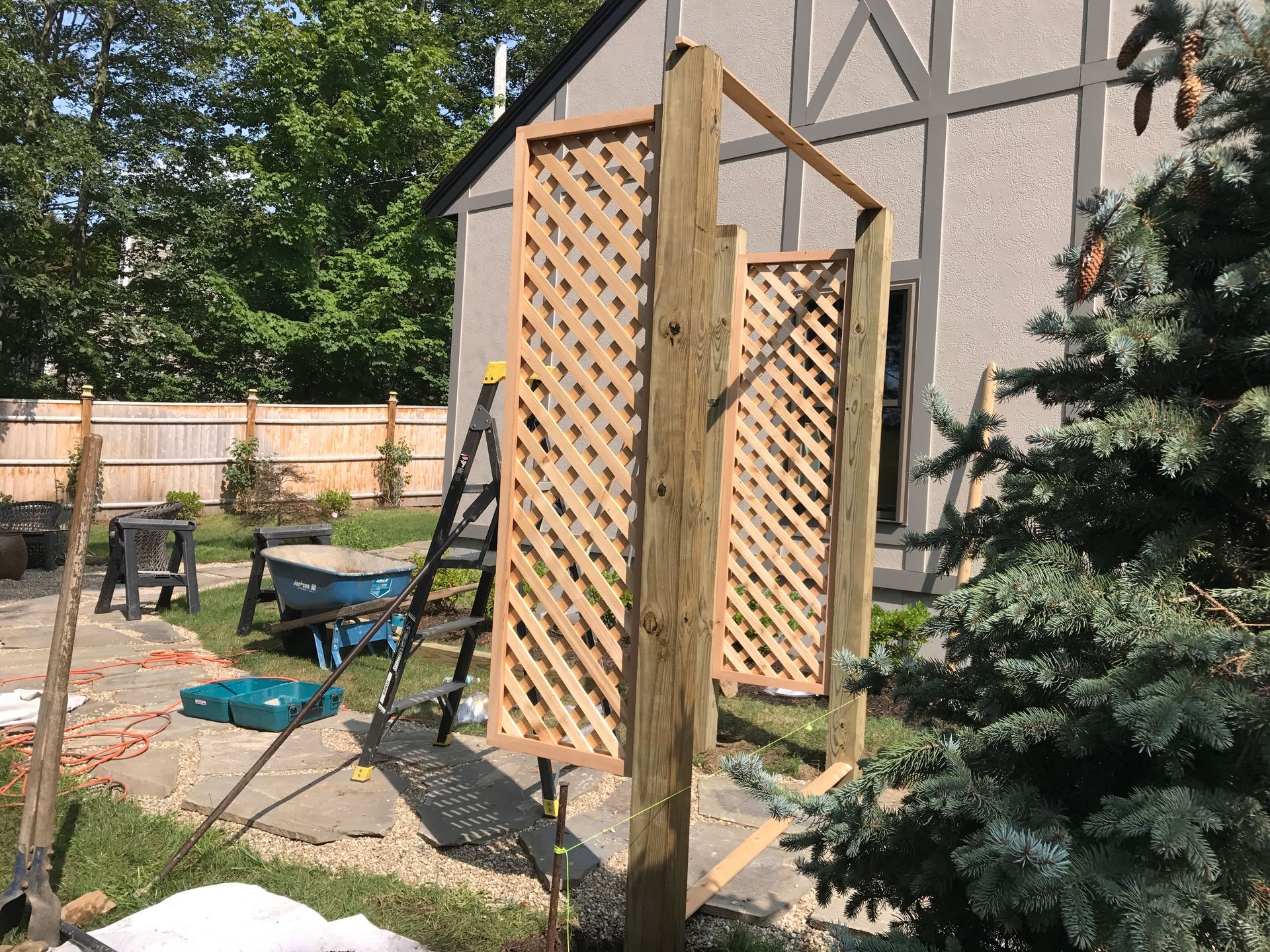 A wooden trellis is being built in a backyard in front of a house.