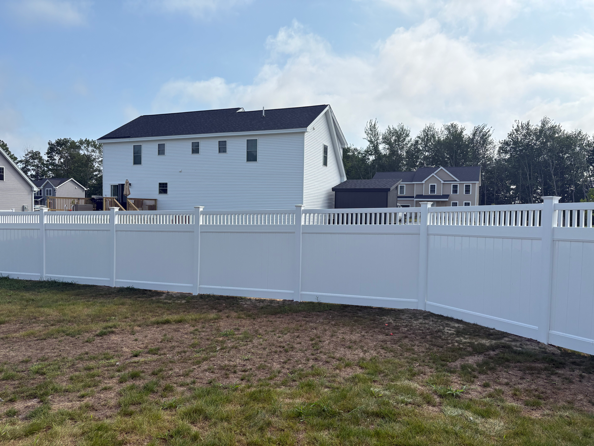 A white fence surrounds a grassy yard in front of a house.