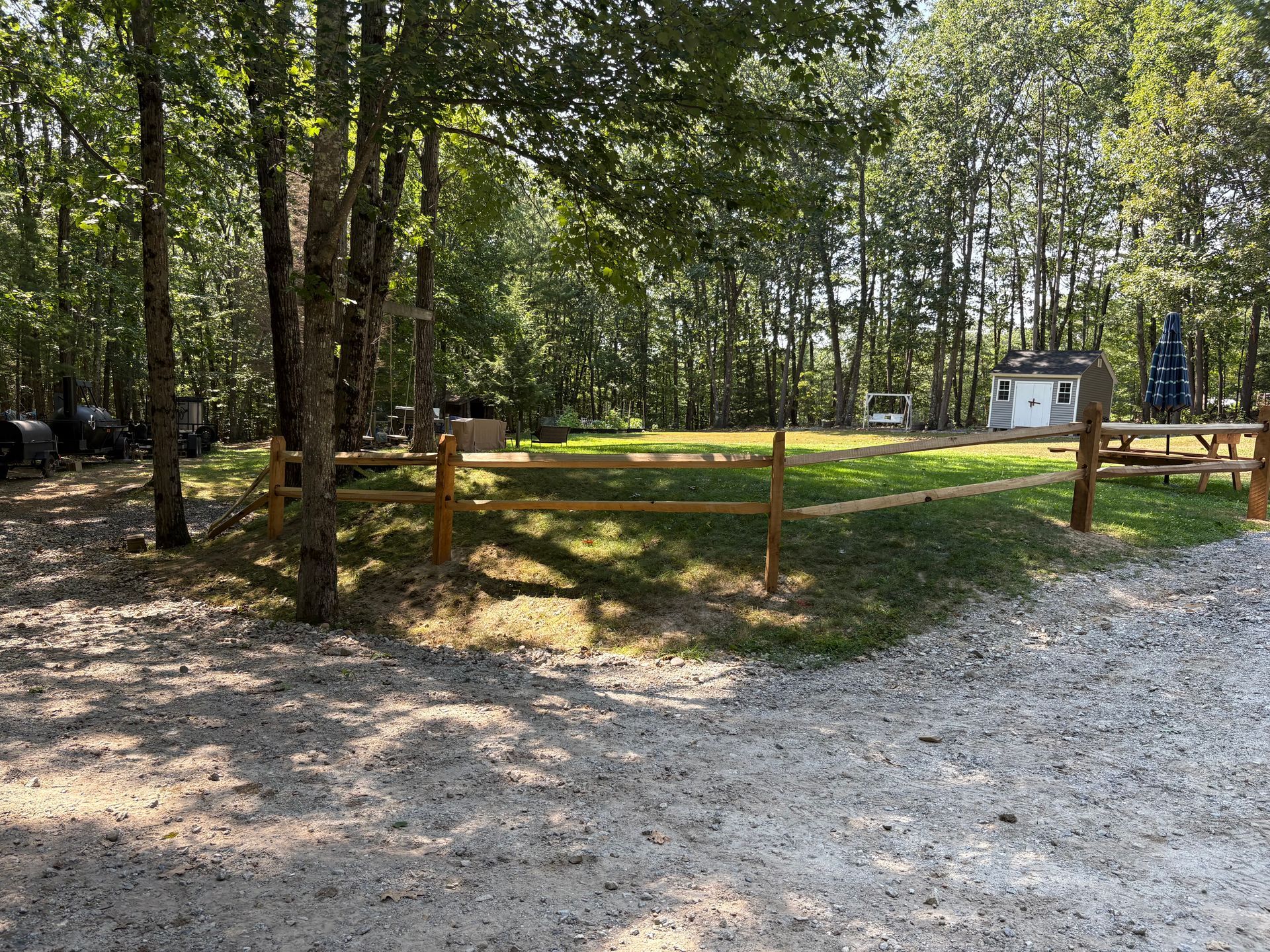 A wooden fence surrounds a grassy area in the middle of a forest.