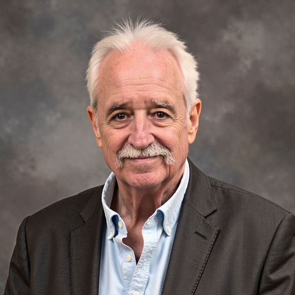 Studio portrait of an older man with white hair and mustache in a dark blazer and light blue shirt