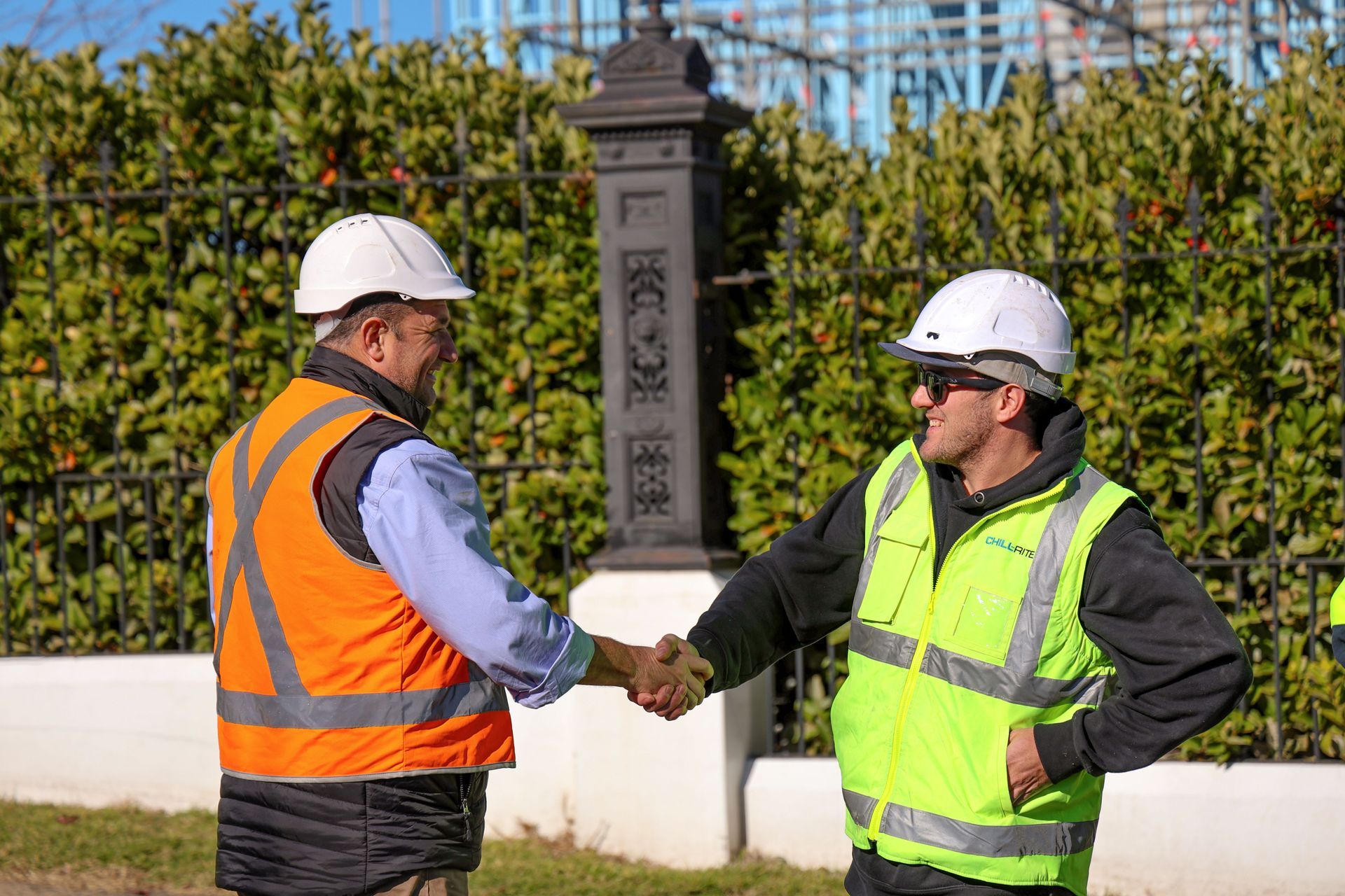 Two construction workers shake hands, both wearing hard hats and safety vests outside a building site— Chill-Rite Refrigeration and Air Conditioning in Coffs Harbour, NSW