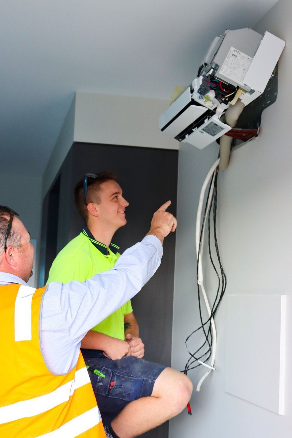 Two Men Are Working on an Air Conditioner on a Wall — Chill-Rite Refrigeration and Air Conditioning in Newcastle, NSW
