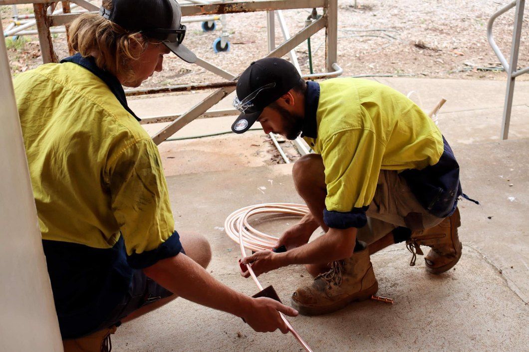 Two Workers in Yellow Shirts Kneel on a Concrete Floor — Chill-Rite Refrigeration and Air Conditioning in Wagga Wagga, NSW