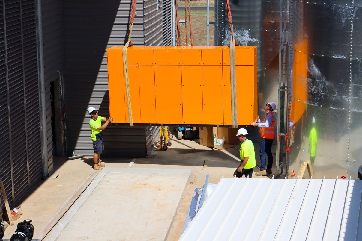 A Group of Construction Workers Are Lifting a Large Orange Box — Chill-Rite Refrigeration and Air Conditioning in Dubbo, NSW