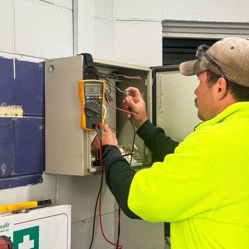 A Man in a Yellow Shirt is Working on an Electrical Box — Chill-Rite Refrigeration and Air Conditioning in Dubbo, NSW