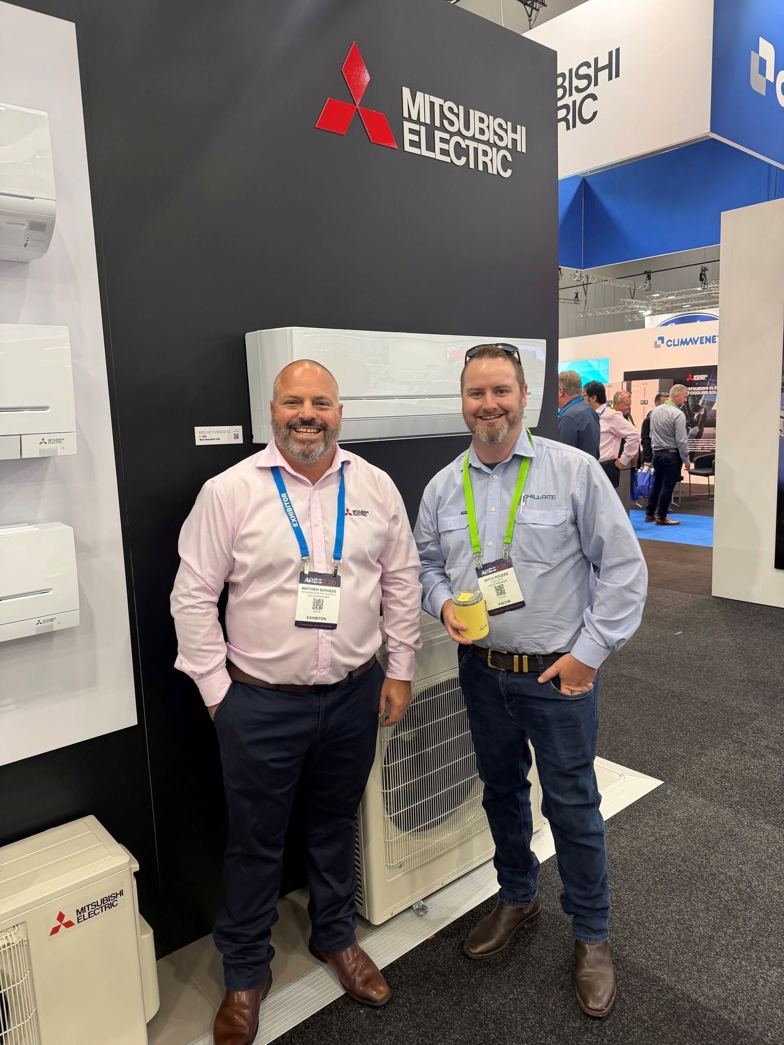 Two Men Posing at A Mitsubishi Electric Booth at A Trade Show — Chill-Rite Refrigeration and Air Conditioning in Wodonga, VIC