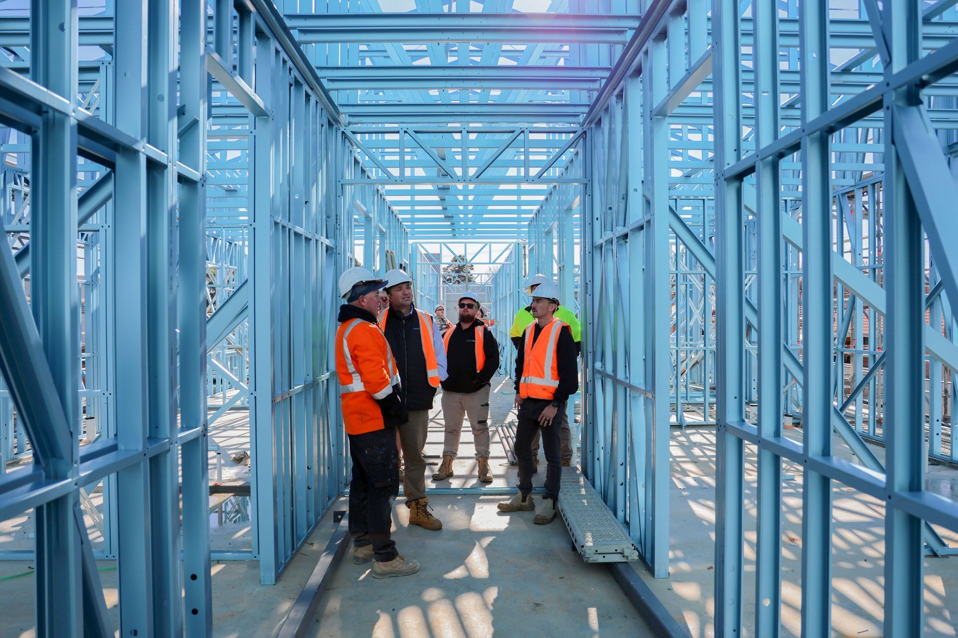 Construction workers in an unfinished steel-frame building, wearing safety vests, conversing— Chill-Rite Refrigeration and Air Conditioning in Newcastle, NSW