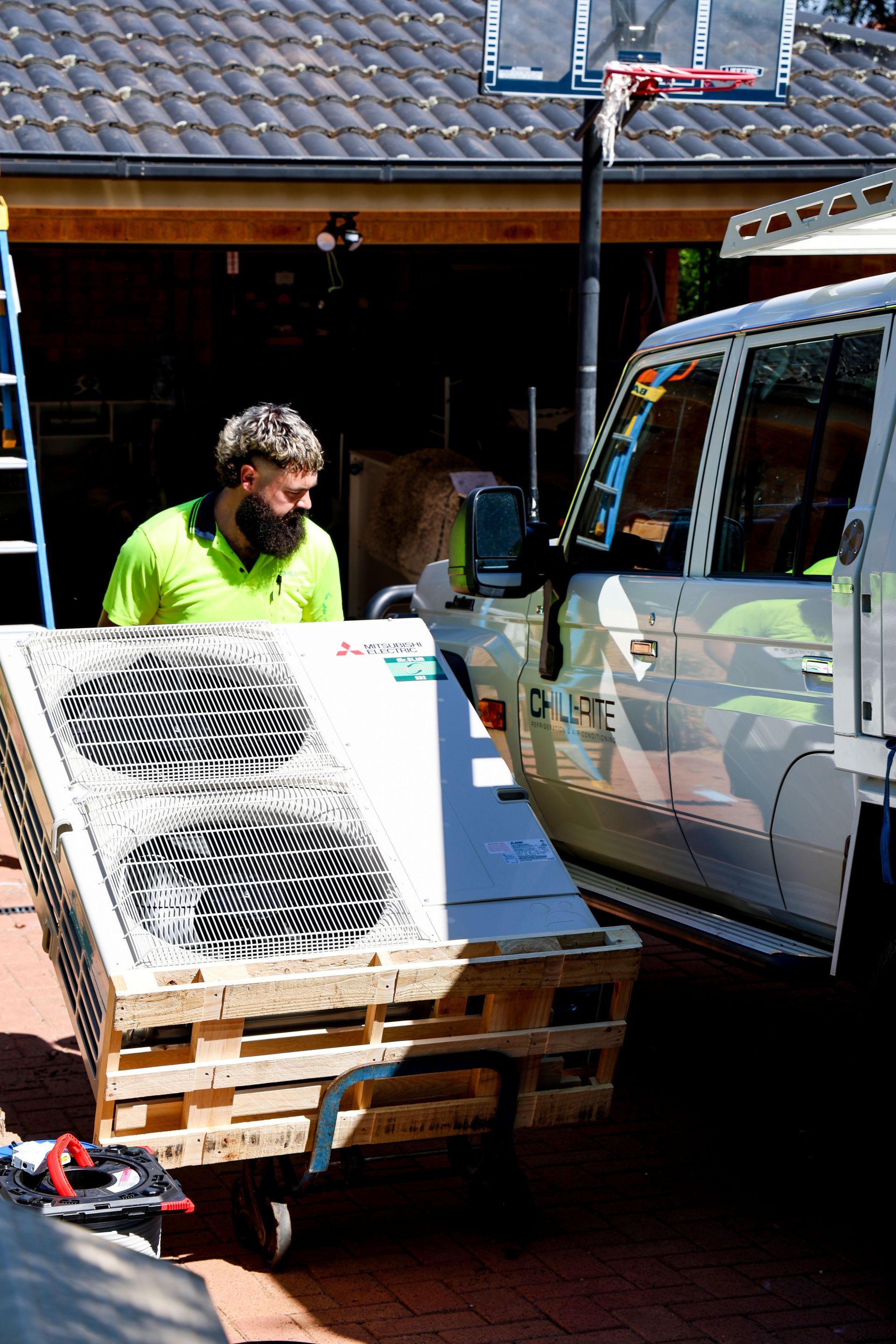 Man rolling a pallet with HVAC units towards a truck in front of a garage— Chill-Rite Refrigeration and Air Conditioning in Dubbo, NSW