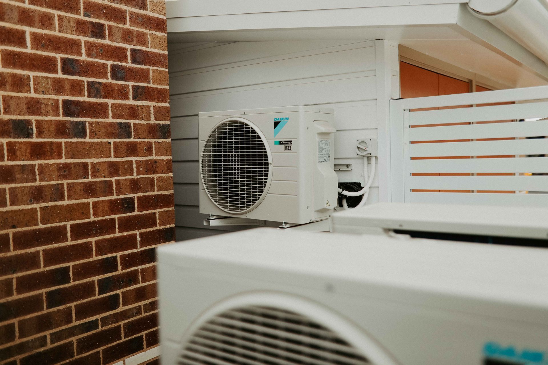 Outdoor air conditioning units mounted on a white wall next to a brick wall— Chill-Rite Refrigeration and Air Conditioning in Newcastle, NSW