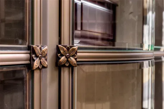 Close-up of a glass elevator with gold butterfly-shaped metal accents on the doors