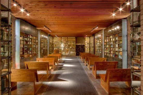 Wood-paneled library interior with rows of bookshelves, wooden benches, and warm ceiling lights