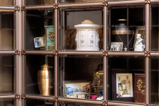Wooden display cabinet with shelves of urns, framed photos, and small decorative objects