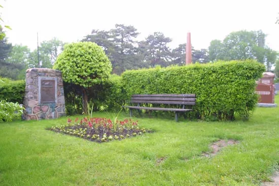 Garden bench beside flower bed and stone plaques in a lush green park