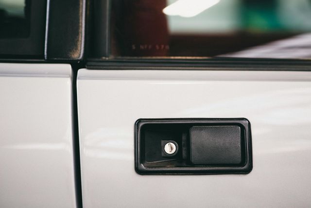 A close-up of a black rectangular car door handle with a visible keyhole on a white car door.