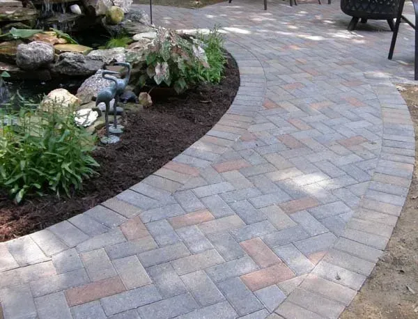 A circular stone fire pit and a stone retaining wall on a paved patio in a residential backyard.