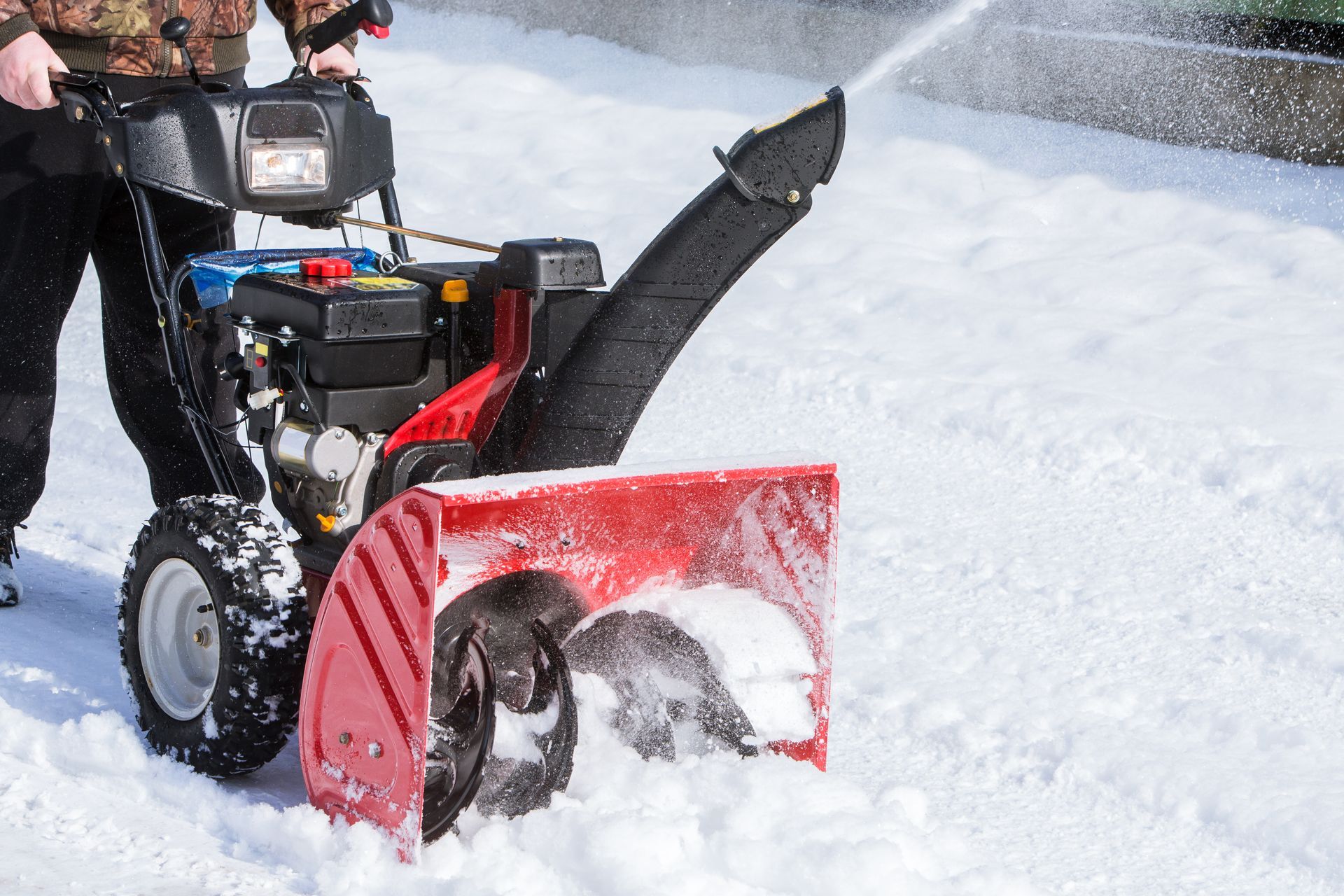 A person operates a bright red snowblower, clearing deep snow on a bright, sunny winter day.