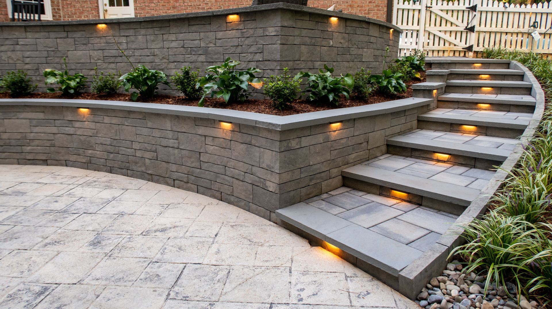 Custom stone retaining wall with integrated cap lighting and tiered patio steps.