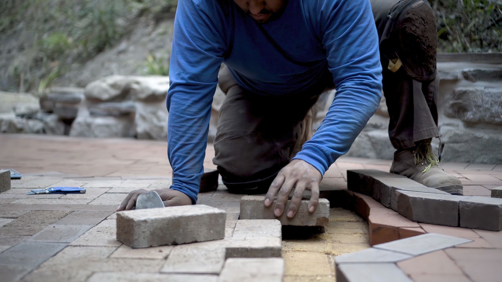 Worker laying concrete pavers by hand on a backyard patio.