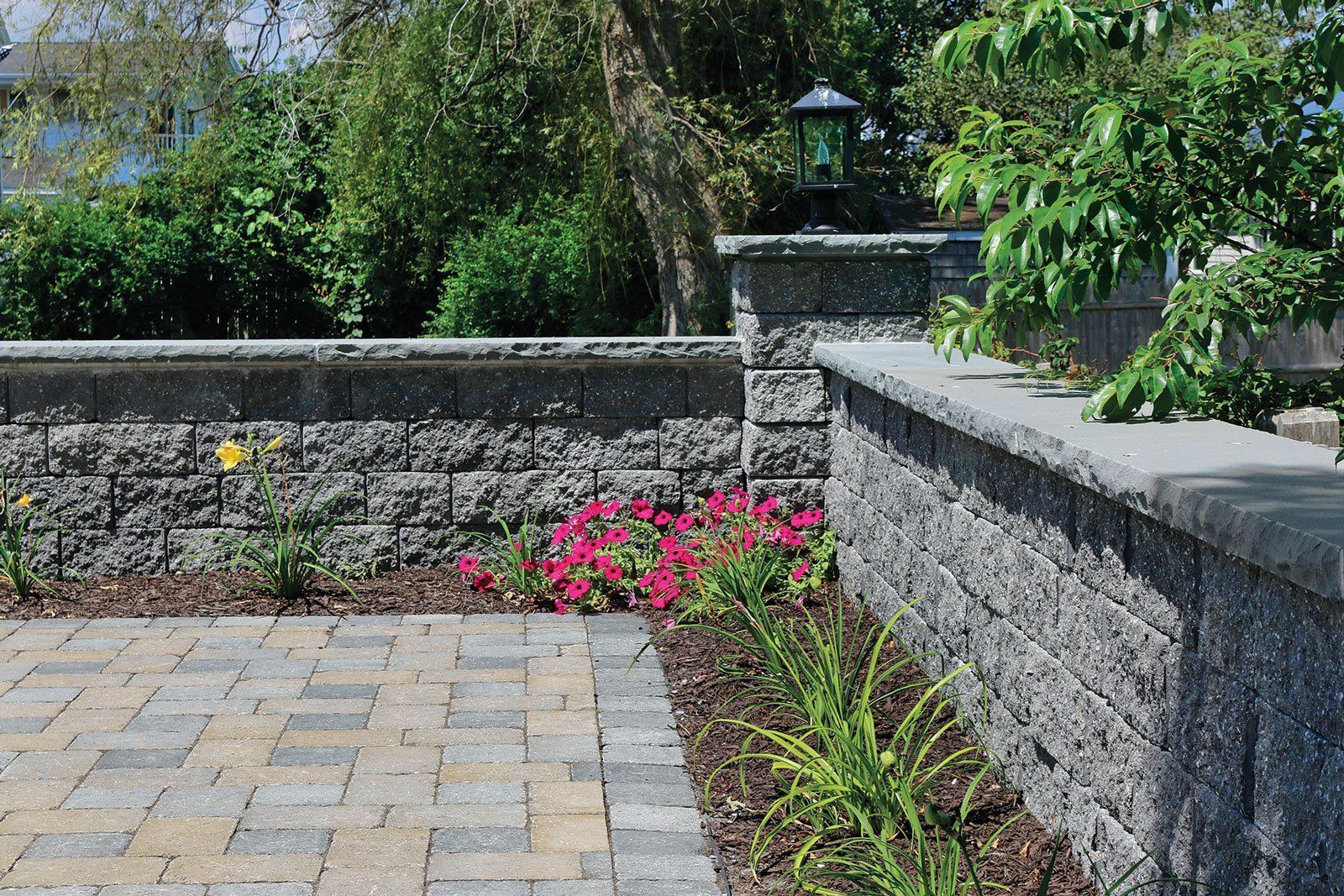 Curved stone retaining walls create terraced garden beds filled with vibrant yellow, orange, and red flowers.