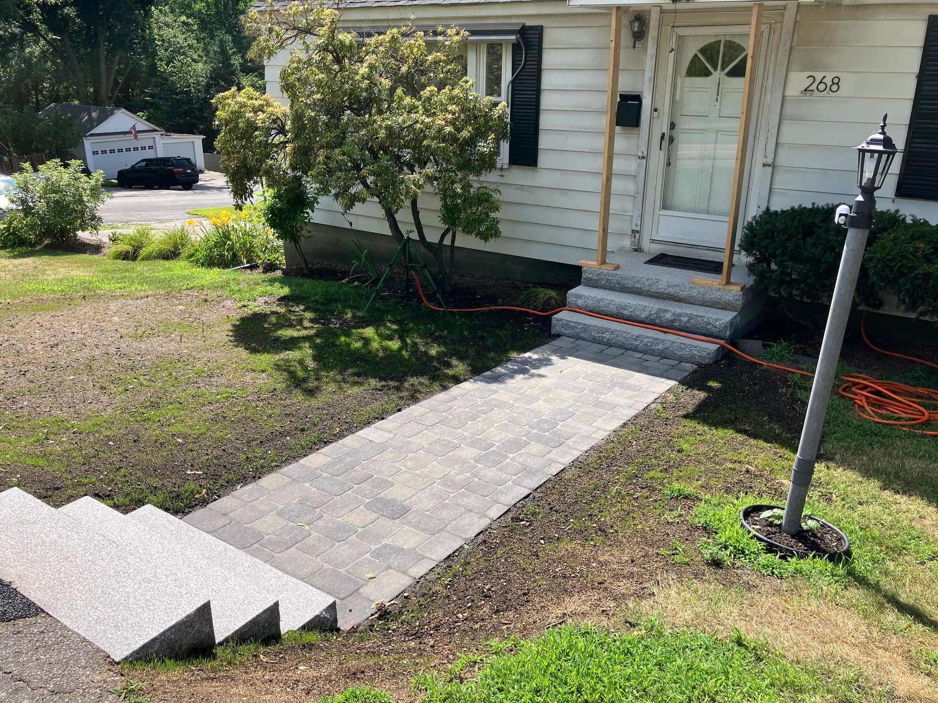 A new stone paver walkway leads to front porch steps of a white house with a grass lawn and a street lamp.