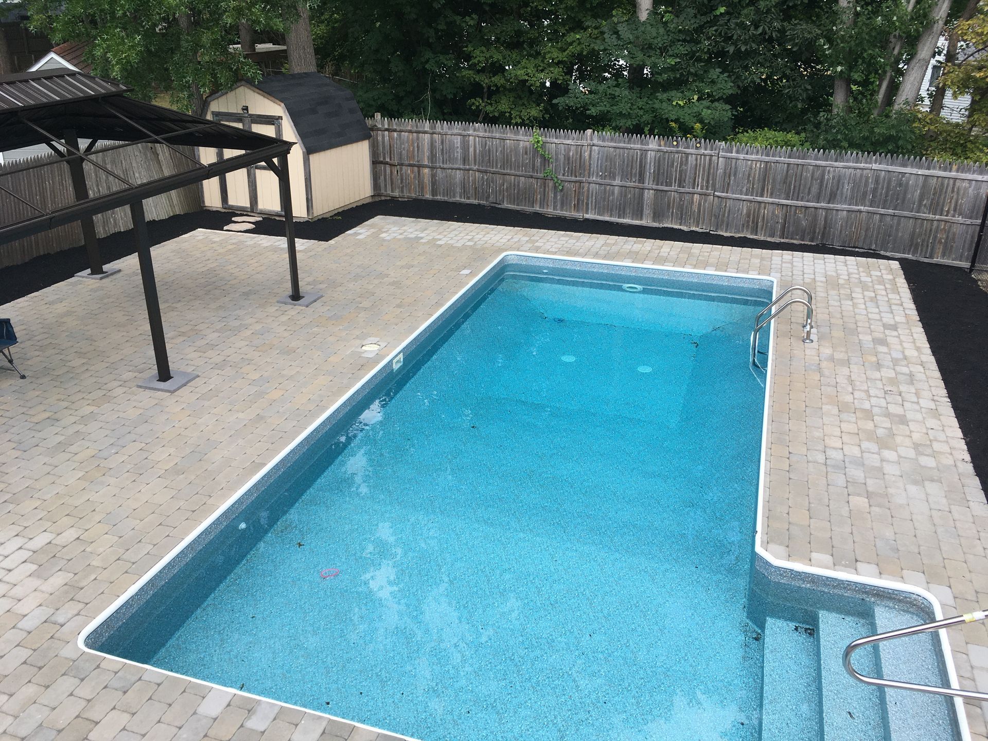 A stone patio with a curved retaining wall and built-in lighting overlooks a wooded area at dusk.