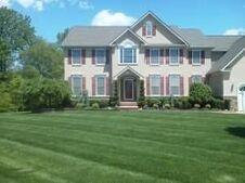 Large two-story house with a green lawn. Light-colored exterior, multiple windows, and a dark roof.