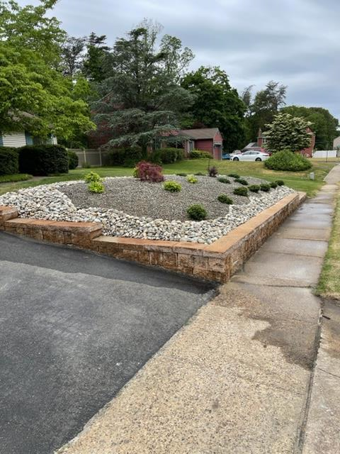 Landscaped rock garden with a low brick retaining wall beside a driveway and sidewalk.